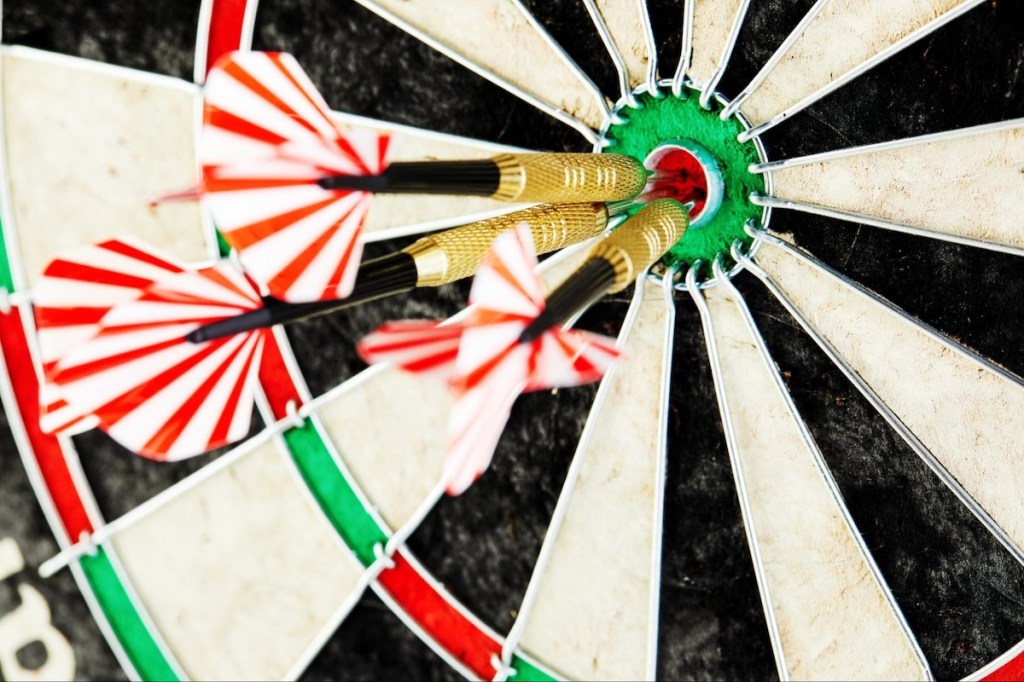 Three-darts-with-red-and-white-flights-hit-bullseye-on-dartboard